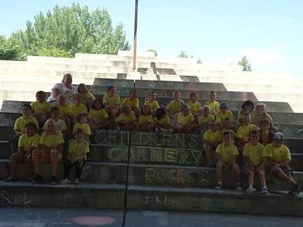 Children's Corner summer camp group on amphitheater steps beside their name written in chalk
